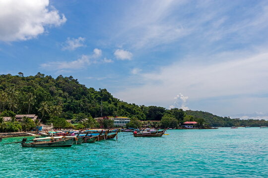 View of vibrant turquoise waters meet lush green hills dotted with traditional longtail boats under a bright sky, Phi Phi Island, Krabi, Thailand.