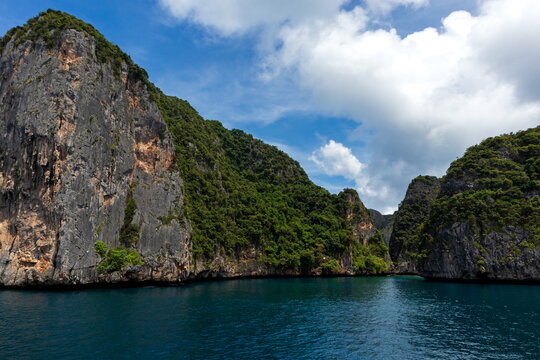 View of towering cliffs draped in vibrant green foliage meet the tranquil turquoise waters under a bright sky, Phi Phi Island, Krabi, Thailand.