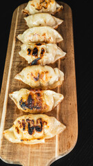 Beautiful pan-fried gyoza arranged on a wooden board, crispy and golden brown. Ready to eat as appetizer or main dish, with soy dipping sauce.