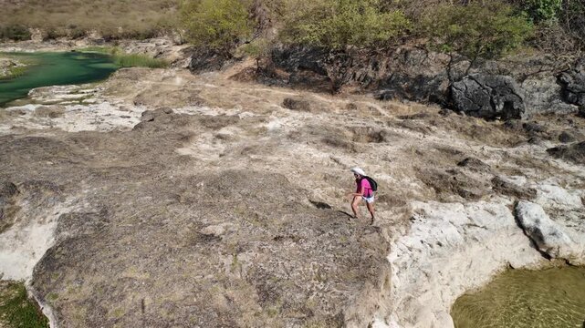 aerial view of tourist woman walking with freedom and happiness in the vibrant green waters and lush landscape of Wadi Darbat, a natural park located near Taqah, Dhofar, Oman