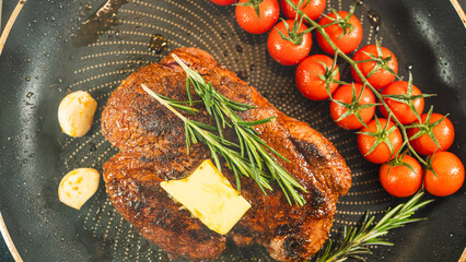 Rare rump steak sizzling in a pan with cherry tomatoes, garlic, and rosemary. Butter melting over the steak, creating a golden crust. Juicy and aromatic cooking process.