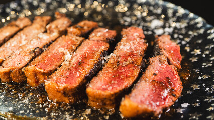 Sliced rare rump steak on a plate, revealing pink interior under a beautiful golden crust. Topped...