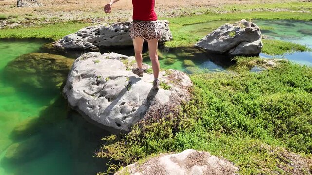 Woman walking in slow motion on rocks, with freedom and happiness in the vibrant green waters and lush landscape of Wadi Darbat, a natural park located near Taqah, Dhofar, Oman