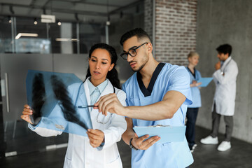 Two young doctors middle-eastern man and woman looking at x-ray scan of patient lungs, discussing...