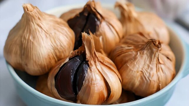 Close up of rich black garlic bulbs in a light blue bowl, culinary ingredient.