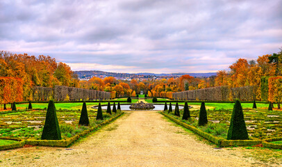 Autumn view of the formal gardens at Chateau de Champs-sur-Marne near Paris in France. Colorful fall foliage and sculpted topiaries line the path leading to a fountain