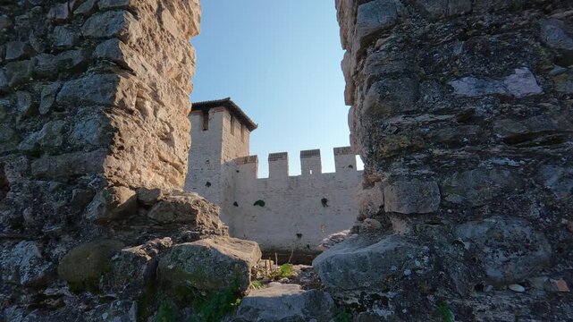 Stabilized left-to-right shot of medieval brick walls and a tower, viewed through a foreground slit in the battlements.
