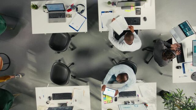 Top down view zoom in of employees engaged in business intel and analytics using data diagrams in office, staff reviews projections and reports to improve overall company strategy. Camera A.