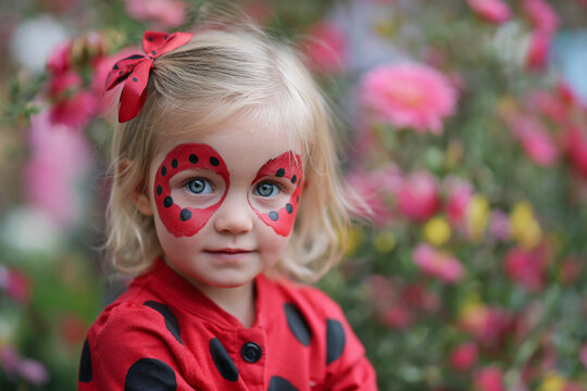 Girl with ladybug face paint surrounded by colorful flowers at a festive outdoor event - Powered by Adobe