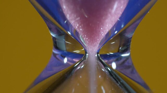 Hourglass, detail of the pink sand passing through the narrow, constricted tube.