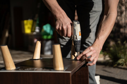 Man Assembling Furniture With Power Drill in Outdoor Space