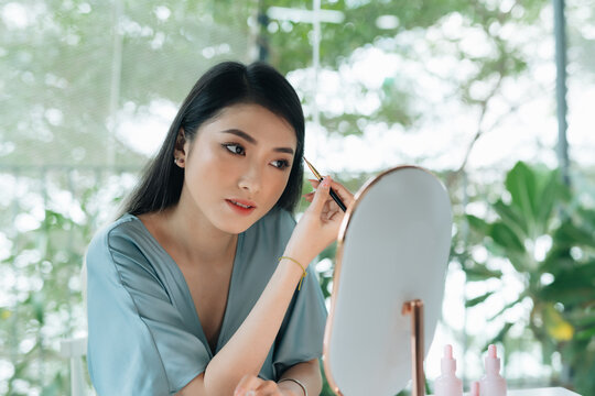 Beautiful young woman with stylish makeup and brush on living room