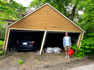 Person Stands by Leaning Garage With Car and Bags in Garden Area