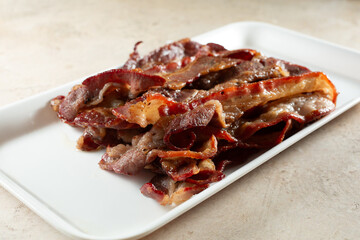 A view of a pile of cooked halal beef bacon, on a tray.