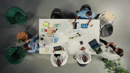 Top down view of physicians and medics gathered for briefing conference. Group discusses healthcare advancements, laboratory research and treatment methods to enhance medical care. Camera A. - Powered by Adobe