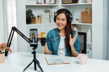 Host channel Asian influencer talking in broadcast wearing headsets on social media live on smartphone recording online, greeting listeners with coaching life or business at modern studio. Stratagem.