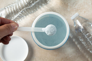 A top down view of a hand gathering a scoop of blue hydration powder from a container.