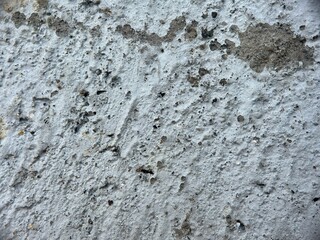 Close-up macro texture of a rough, weathered light grey concrete or cement surface with dark pitting and imperfections.