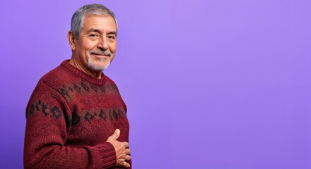 Happy senior Hispanic man with a grey beard and patterned red sweater smiling confidently against a vibrant purple studio background