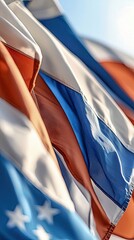 Close-up of several flags waving in the wind on a sunny day. The flags are a mix of colors, including red, white, blue, and some with stars.