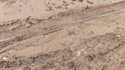 Muddy ground texture with deep tire tracks and wet soil patterns, showing natural rough terrain and dirt surface details. Ideal for backgrounds, environmental concepts, construction themes