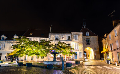 Night view of the historic Gate of Garlande Castle in Tournan-en-Brie, Paris Region of France. The medieval stone gatehouse with a clock tower is illuminated under a dark sky