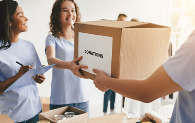 A group of volunteers is organizing donations for a charity event. They are smiling and passing a...