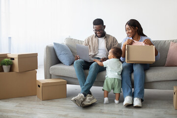 Joyful family of three enjoys quality time in their new home, using a laptop and organizing boxes...