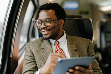Man Sitting Inside Train Observing Outside View While Using Tablet