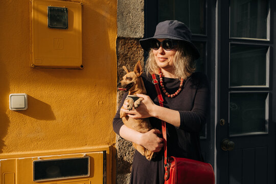 Woman in sunhat holding Miniature Pinscher by yellow wall