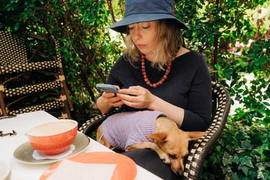 Woman at cafe with dog on lap browsing smartphone