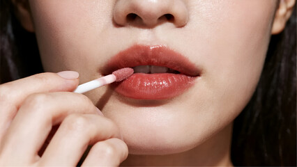 Close-up of a person applying shiny lip gloss to their lips. Perfect for beauty, makeup, skincare, and cosmetics concepts.