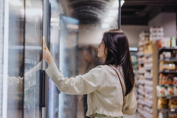 Woman shopping in supermarket freezer aisle