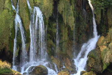 Scenic view of the Kravica Waterfall in Herzegovina, featuring multiple cascading streams flowing over lush green cliffs into a clear pool below.