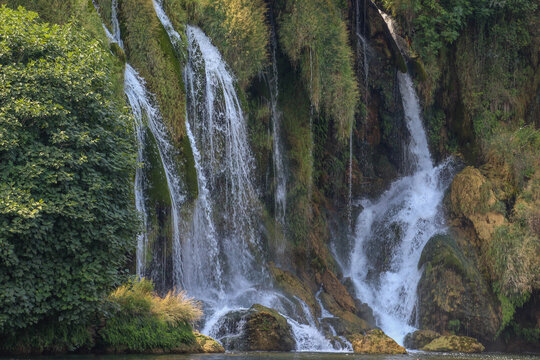 A peaceful waterfall cascading over moss-covered rocks surrounded by dense greenery, creating a refreshing and serene natural landscape.