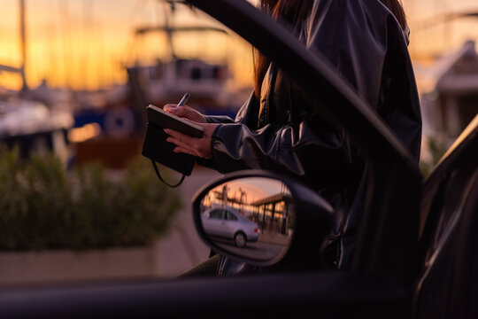 Woman Writing in a Notebook at Sunset Near Car