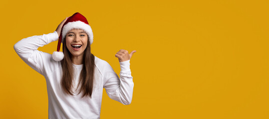 A girl wearing a red and white holiday hat smiles brightly while giving a thumbs up. She stands...