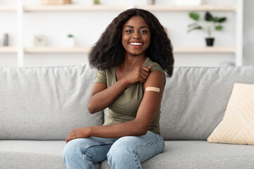 A young woman sits comfortably on a gray couch in her living room. She smiles as she lifts her...