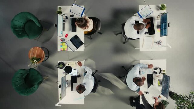 Top down view of professional diverse staff analyzing finance numbers and documents in a business workspace. Team discusses reporting, market research and resource allocation. Camera A.