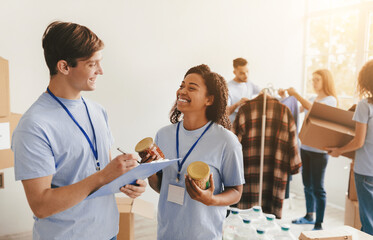 A group of volunteers sorts food donations in a community center. Two individuals smile while...