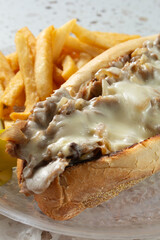 A view of a Philly cheesesteak with some french fries.