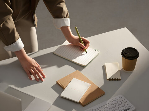 A person's hands writing in a notebook at a desk with coffee