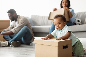 A joyful African American family is relocating to a new apartment. A small child plays with...