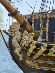 Elaborate carvings of a lion and angels adorn the back of an old ship near the water