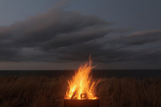 Fire Burning in a Metal Grill Near the Water at Dusk