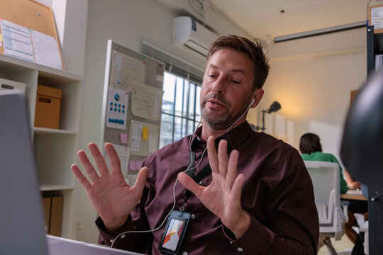 Man with headset gesturing during video call in office.