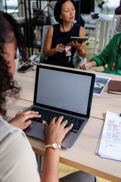 Office scene, woman types on laptop during a meeting.