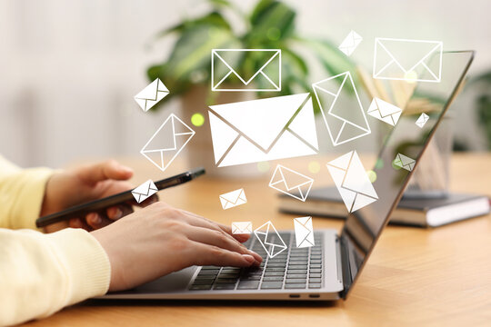 Email notification. Woman using laptop and mobile phone at table, closeup. Letters flying out of screen