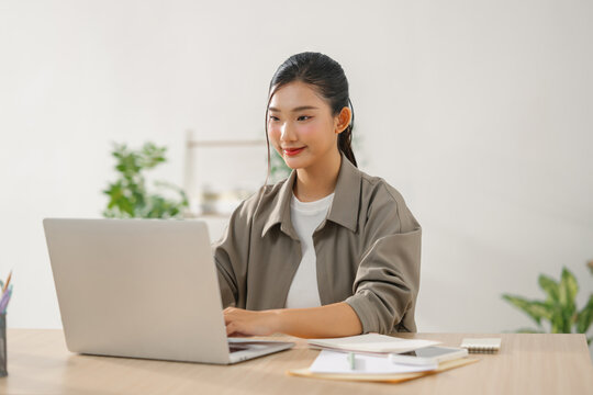 A young Asian woman is using her laptop at her desk