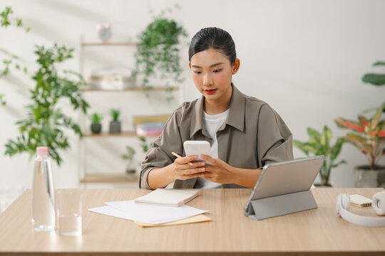 Asian woman using smartphone at a desk with a digital tablet - Powered by Adobe